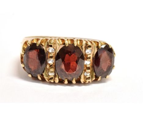 A 9CT GOLD, GARNET THREE STONE DRESS RING The faceted oval garnets measuring approx. 0.7cm X 0.5cm each with crystal glass ac