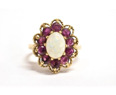 A 9CT GOLD PINFIRE OPAL AND GARNET GLASS FLOWER HEAD RING The central oval opal measuring 0.7cm x 1.5cm with the flower head 