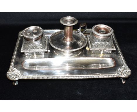 A SILVER PLATED COPPER DOUBLE INKWELL AND CANDLE HOLDER STAND The stand on four feet with shell pattern to the corners and ri