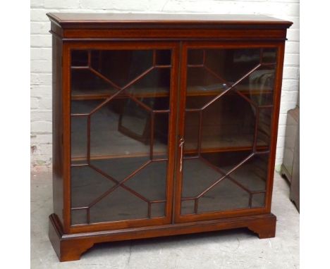 An Edwardian inlaid mahogany bookcase, the twin astragal glazed doors enclosing two adjustable shelves, raised on bracket fee