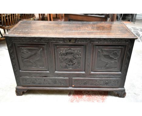 An 18th century carved panelled oak coffer, the front with stylised carved detail of birds and mask head above two drawers, r