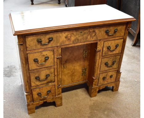 A reproduction burr walnut veneered knee hole desk with single long drawer above six short drawers and central cupboard door,