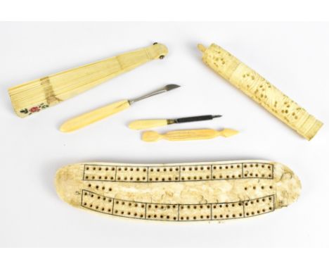 A late 19th century carved walrus tooth cribbage board, length 24cm, a foliate carved bone needle case with needles, two carv