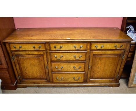 A reproduction oak sideboard with cross banded detail and four central drawers flanked by two further drawers, raised on brac