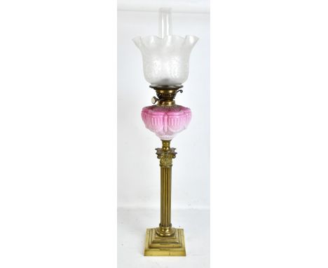 A Victorian brass Corinthian column oil lamp with pink glass reservoir featuring relief decoration and frosted glass shade, h