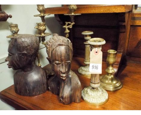 A pair of two branch brass candelabra, pair of candlesticks, two native carved busts and one other candlestick 