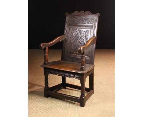 A 17th Century Joined Oak Wainscot Chair.  The shaped cresting rail carved with scrolling foliage above a carved frieze and f