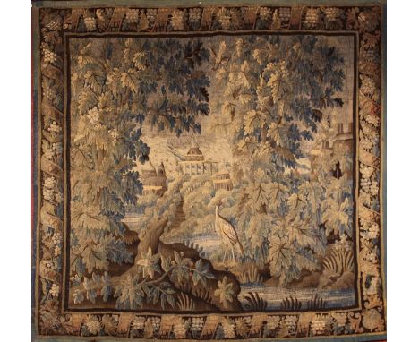 A 17th Century Verdure Tapestry depicting a park landscape with a wading bird by stream in foreground and turetted buildings 