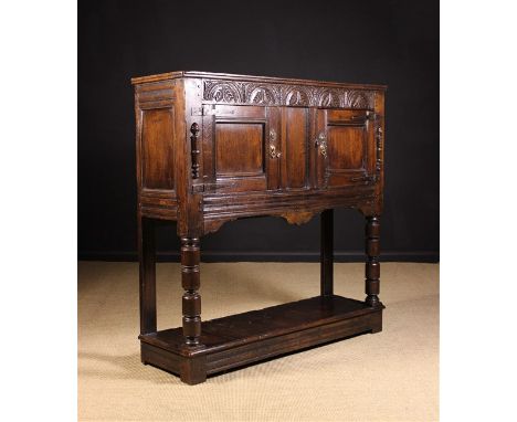 A 17th Century Livery Cupboard. The planked top above a lunette carved frieze rail and moulded panel doors flanked by split s