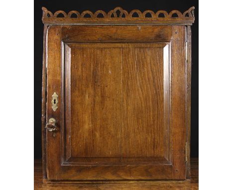 An 18th Century Oak Wall Cupboard. The top surmounted by a pierced & scalloped gallery rail. The fielded panel door opening t