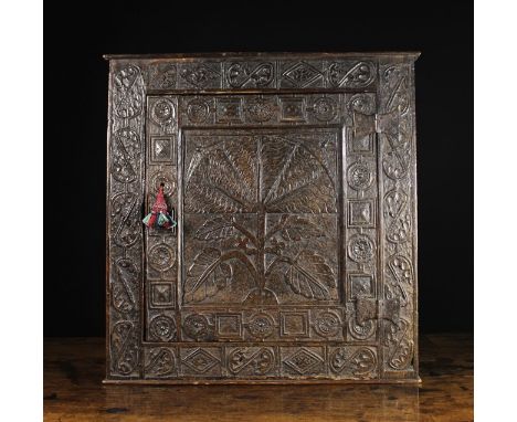 A 17th Century Carved Oak Mural Cupboard. The panel door decorated with a flowering plant issuing a fanned bloom of scalloped