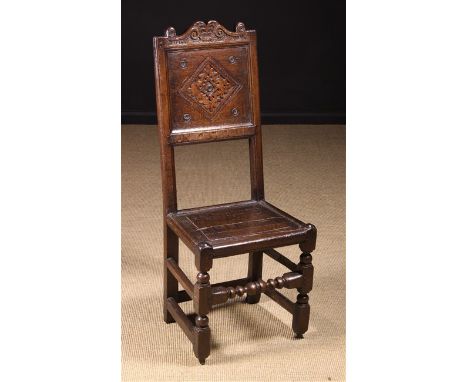 A Late 17th Century Oak Back Stool. The shaped cresting rail enriched with S-scrolls & scale carving above a panel back with 