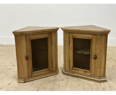 A pair of Edwardian pine wall mounted corner cabinets with glazed panel doors and single shelf, on moulded base