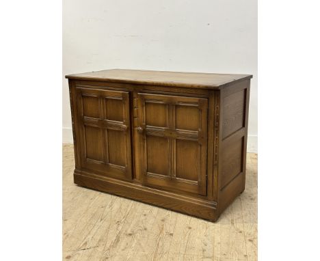An Ercol oak side cupboard with rectangular top above a pair of inset panel doors enclosing a shelf with turned wood handles 