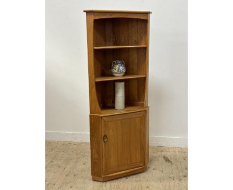 An Ercol light elm floor standing corner cabinet with moulded top and three open shelves and panel door with two interior she