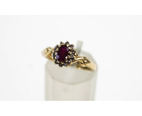 A 9 carat gold ruby and diamond cluster ring, the oval cut enclosed by twelve single cuts, finger size L, 2.9 g gross