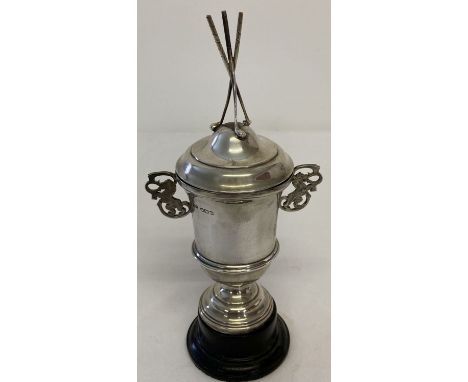 A vintage silver lidded trophy cup with 3 golf club finial to top and pierced work lion handles. With a black wooden stand. H