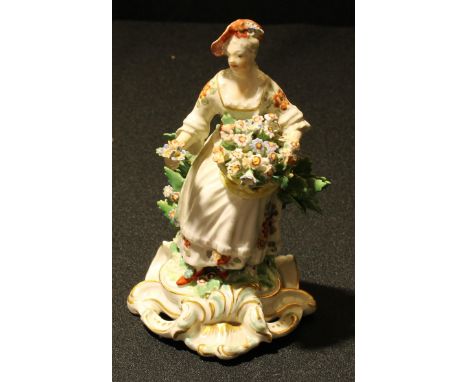 A rare Derby Patch Mark figure, Allegorical of Spring, seated holding a basket of flowers, before bocage, pierced scroll base