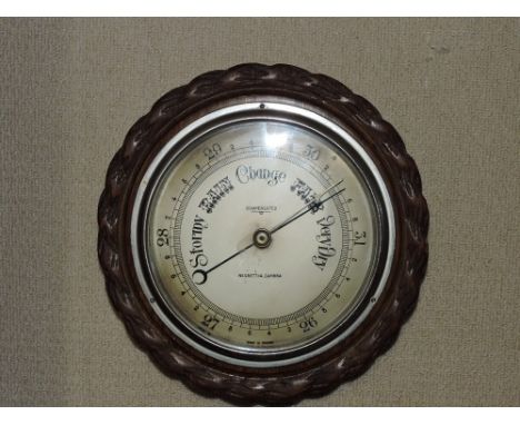 An oak framed circular aneroid barometer, by Negretti & Zambra, silvered dial within a carved frame, D. 24cm.
