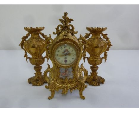 A French gilded metal mantle clock with porcelain panels and vase form garnitures