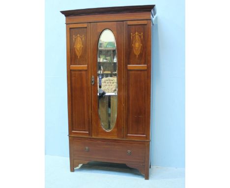 An Edwardian inlaid mahogany wardrobe, the single door with an oval mirror, above a single long drawer and raised on shaped b