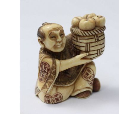 A Japanese Meiji Period Carved and stained Ivory Netsuke figure of a man seated cross-legged with a basket of fruit balanced 