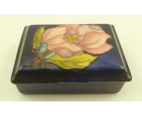 A MOORCROFT CERAMIC TRINKET BOX, of rectangular form, the lid tube lined and painted with a magnolia design in pink on a coba