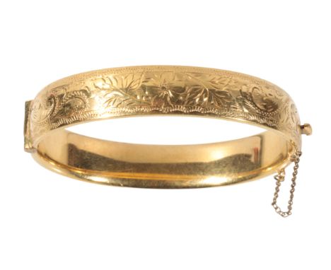 A 9CT GOLD HINGED BANGLE with half engraved decoration and attached safety chain, (c. 20grams)