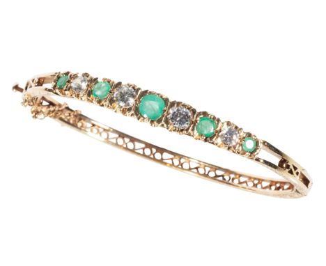 A 9CT GOLD BANGLE set with clear and green stones, with an attached safety chain, (c.13.0 total weight)