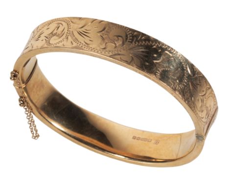 A 9CT GOLD HINGED BANGLE with engraved decoration, and attached safety chain, (c.16.3grams)