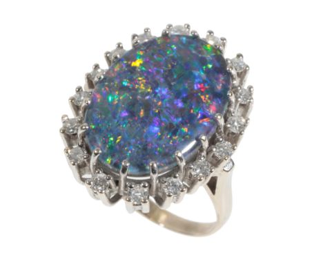 A BLACK DOUBLET OPAL AND DIAMOND RING the central opal with blue, green and red hues, set within a border of brilliant-cut di