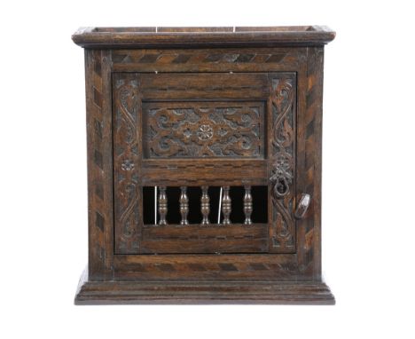 AN OAK MURAL CUPBOARD PROBABLY WEST COUNTRY inlaid with bog oak and holy chevron banding, the hinged door with a relief carve