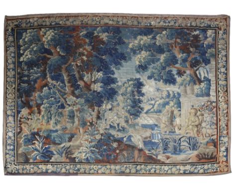 A BRUSSELS VERDURE TAPESTRY LATE 17TH CENTURY worked with figures, in a landscape with cranes and a lake, within a floral bor