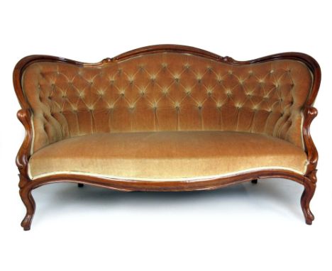 A Victorian mahogany two seat sofa upholstered in a gold button back cut fabric, with a carved and moulded show frame on cabr