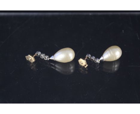 A pair of large pearl and diamond drop earrings, the pearl drop mounted in white metal with graduating three diamond drop wit