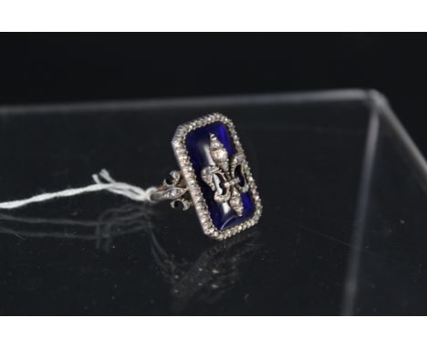 A continental diamond and enamel ring, the large rectangular blue enamelled centre with applied white metal diamond encrusted