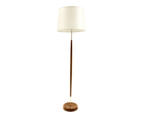 A teak standard lamp,1950s, with a turned shaft, on a concave circular base, with brass fittings, with original paper drum sh