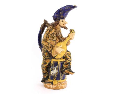 An Émile Gallé faience pitcher, c.1890, in the form of a minstrel with a lute sat on a drum, signed 'E Gallé Nancy' under the