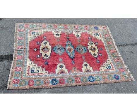 A large hand knotted woollen carpet with geometric designs on a red ground within a multi-border, 300 x 400cm.