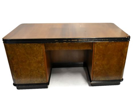 An Art Deco walnut veneered and ebonised twin pedestal desk, the front with single drawer flanked by twin cupboard doors, the