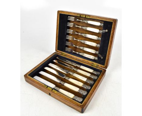 An oak cased set of twelve mother of pearl handled knives and forks with silver plated repousse foliate decorated mounts, bea