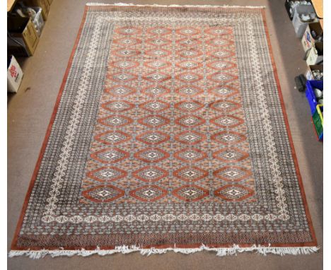 A large hand knotted woolen Bokhara-type carpet with geometric medallions on a peach ground, 382 x 275cm.