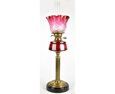 A brass oil lamp with crimped cranberry glass shade, clear chimney and ruby glass reservoir on circular base, height 72cm (sh