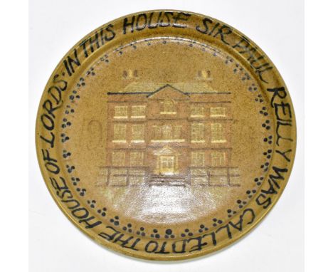 A studio pottery plaque featuring a house to centre with date 1978 and inscription to rim 'In this House Sir Paul Reilly was 