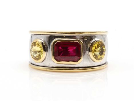 An 18ct two colour gold ruby and yellow sapphire band ring, an emerald cut ruby, rub set in landscape orientation, with a rou