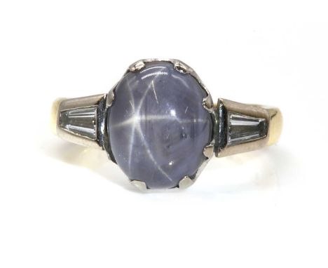 An 18ct yellow and white gold single stone star sapphire ring,with diamond set shoulders. An oval cabochon star sapphire, wit