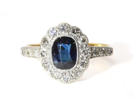 A sapphire and diamond oval cluster ring, c.1930,with an oval mixed cut sapphire, milligrain set to the centre. A border of e