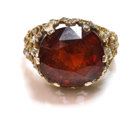 A single stone hessonite garnet ring,with a diamond set mount, the slightly oval mixed cut garnet, claw set to a pierced foli