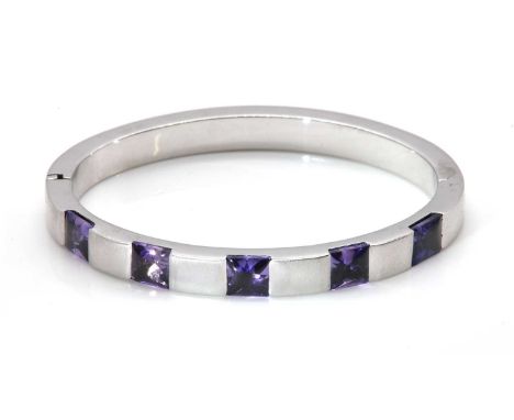 A sapphire set hinged bangle,of oval flat section form, 6.80mm wide, with a series of square, buff top sapphires, end set acr