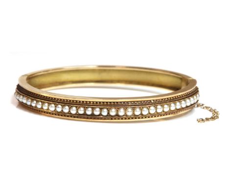 A Victorian Etruscan revival split pearl flat section hinged bangle, c.1870,with a central row of split pearls to the top hal
